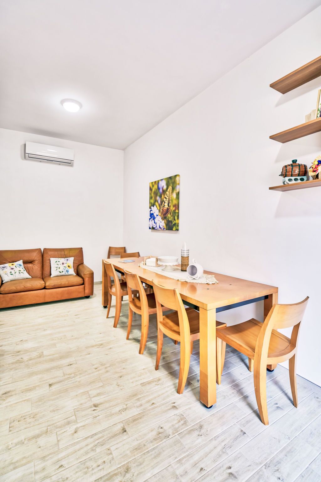 Une pièce comprenant une table à manger en bois, des chaises, un canapé et un climatiseur fixé au mur.