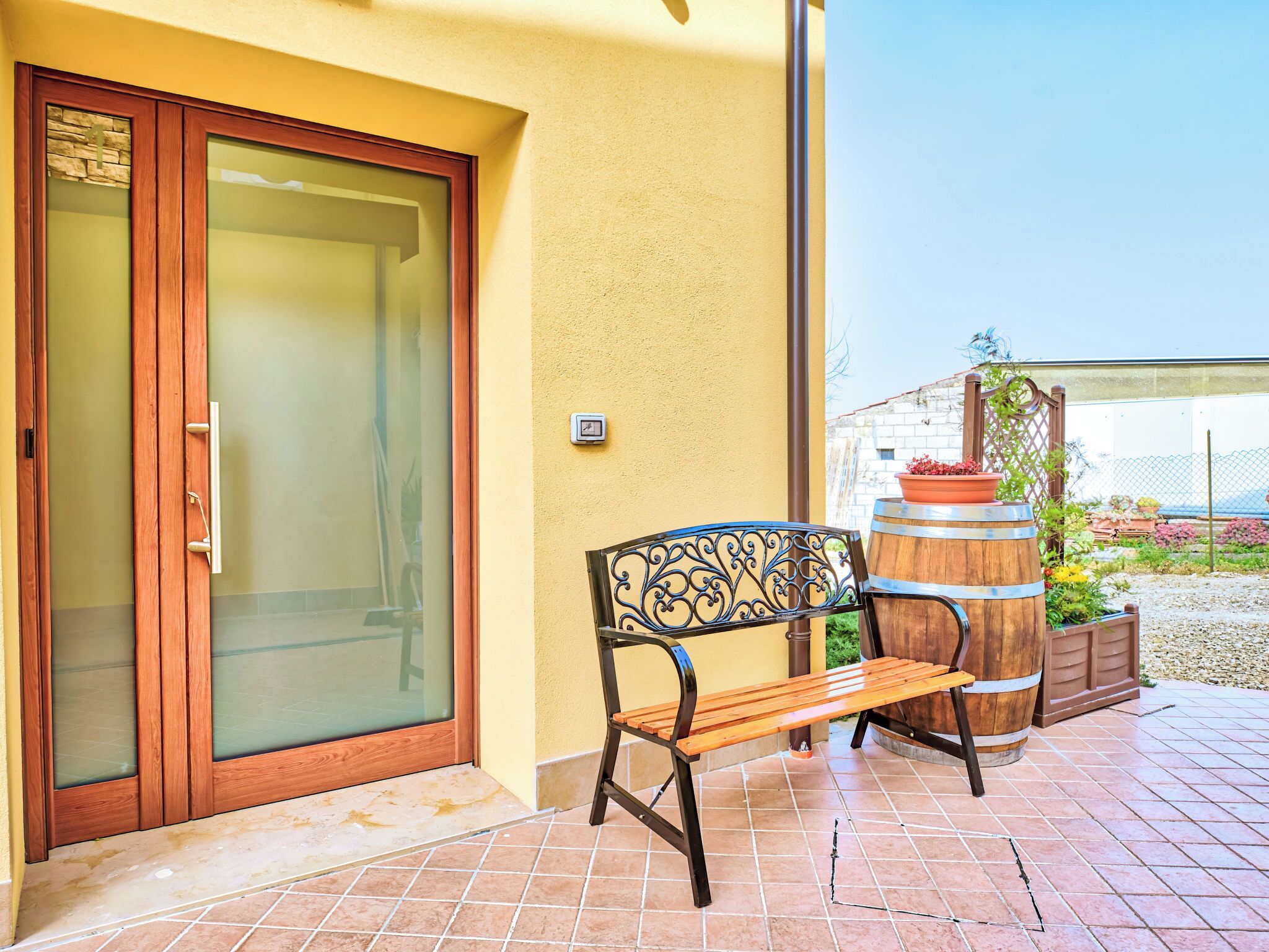 Une terrasse avec un banc, un tonneau en bois et une porte dont les panneaux sont en verre dépoli.