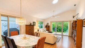 A spacious living area with a dining table, chairs, a sofa, a bookshelf, and a ceiling fan. - Seawoods Beach Retreat - Walk to Beach + Pools (New Smyrna Beach)