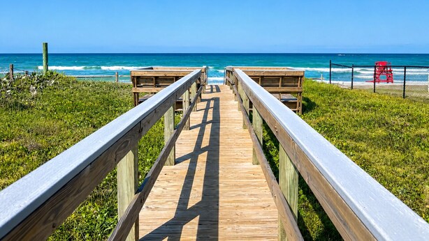 A wooden boardwalk leading to a beach with a lifeguard tower. - Seawoods Beach Retreat - Walk to Beach + Pools (New Smyrna Beach)