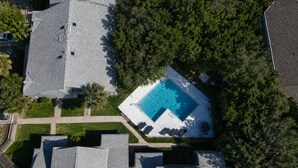 An aerial view of a residential area with a swimming pool surrounded by trees and houses. - Seawoods Beach Retreat - Walk to Beach + Pools (New Smyrna Beach)