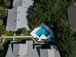 An aerial view of a residential area with a swimming pool surrounded by trees and houses. - Seawoods Beach Retreat - Walk to Beach + Pools (New Smyrna Beach)