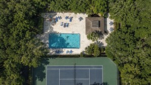 An aerial view of a property with a swimming pool, tennis court, and lounge area surrounded by trees. - Seawoods Beach Retreat - Walk to Beach + Pools (New Smyrna Beach)
