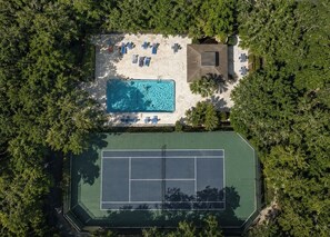 An aerial view of a property with a swimming pool, tennis court, and lounge area surrounded by trees. - Seawoods Beach Retreat - Walk to Beach + Pools (New Smyrna Beach)