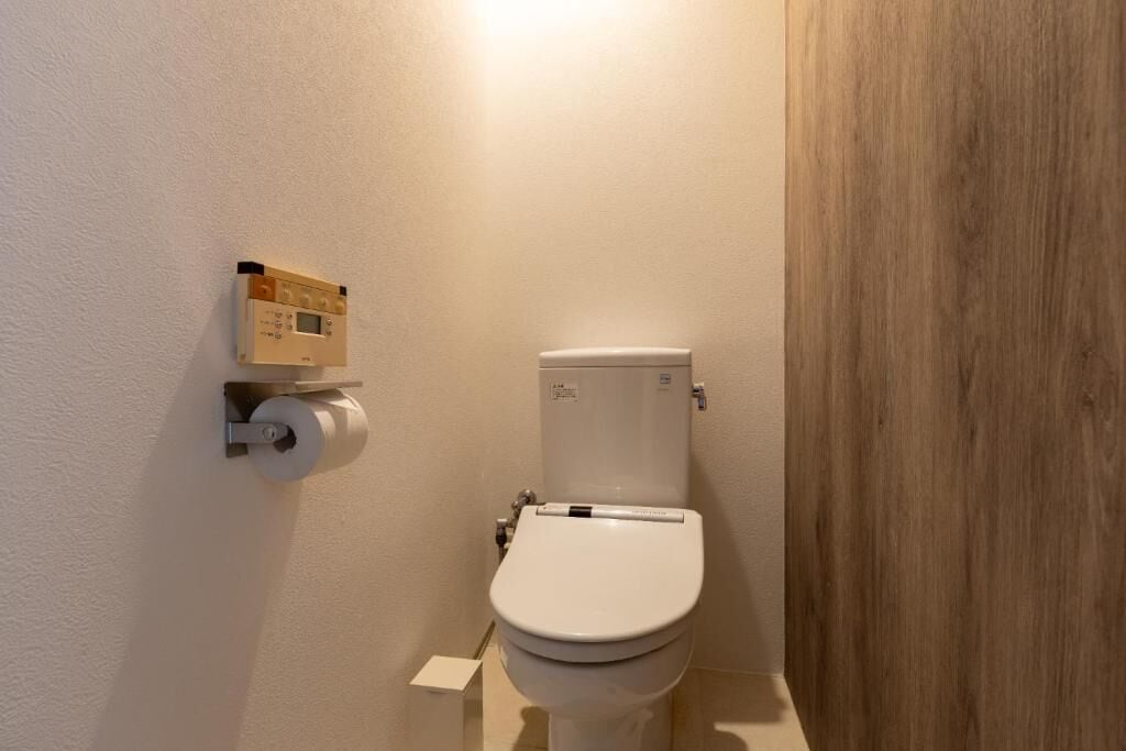A bathroom with a toilet, a toilet paper holder, and a wall-mounted control panel.