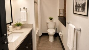 A modern bathroom with a sink, toilet, and shower. There is a towel rack, a framed picture on the wall, and a small plant on the counter. - Brick & Bed - Arch, Riverfront, Convention Center, T-303 (St. Louis)