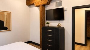 A bedroom with a bed, a black dresser, a mounted TV, and wooden beams on the ceiling. - Brick & Bed - Arch, Riverfront, Convention Center, T-303 (St. Louis)