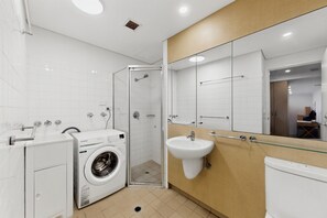 A modern bathroom with a glass shower enclosure, a washing machine, and a sink. - Bright 1-bed Apartment in Neutral Bay (Sydney)
