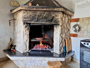 A stone-built kitchen with a built-in grill, a stove, and a hanging pot rack. - Nadalina by Interhome (Šibenik)