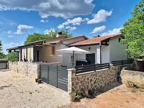 A house with a stone wall, a gated entrance, and a patio area with a table and umbrella. - Nadalina by Interhome (Šibenik)
