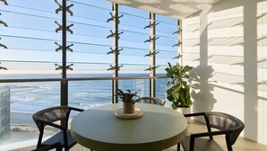 A balcony with a glass railing, a round table, two chairs, and a potted plant. - Lumara Holiday Apartment at Newcastle Beach (Newcastle)