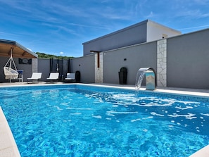 Ein Schwimmbecken mit Wasserspiel, Liegestühlen und einem modernen Gebäude mit Steinwand.