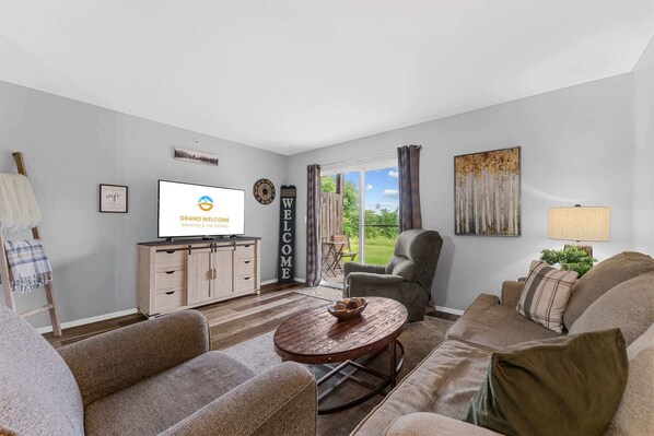 Ein Wohnzimmer mit einer Sofagarnitur, einem Couchtisch, einem Fernseher und Blick ins Freie.