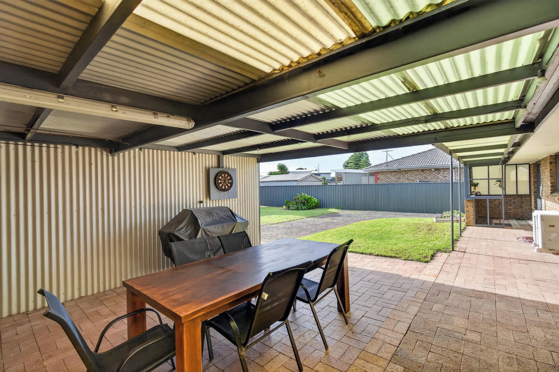 An outdoor patio with a wooden table and chairs, a grill, and a dartboard.