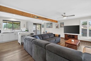 Ein modernes Wohnzimmer mit Küche, einem grauen Ecksofa, einem Holztisch und einem Flachbildfernseher.