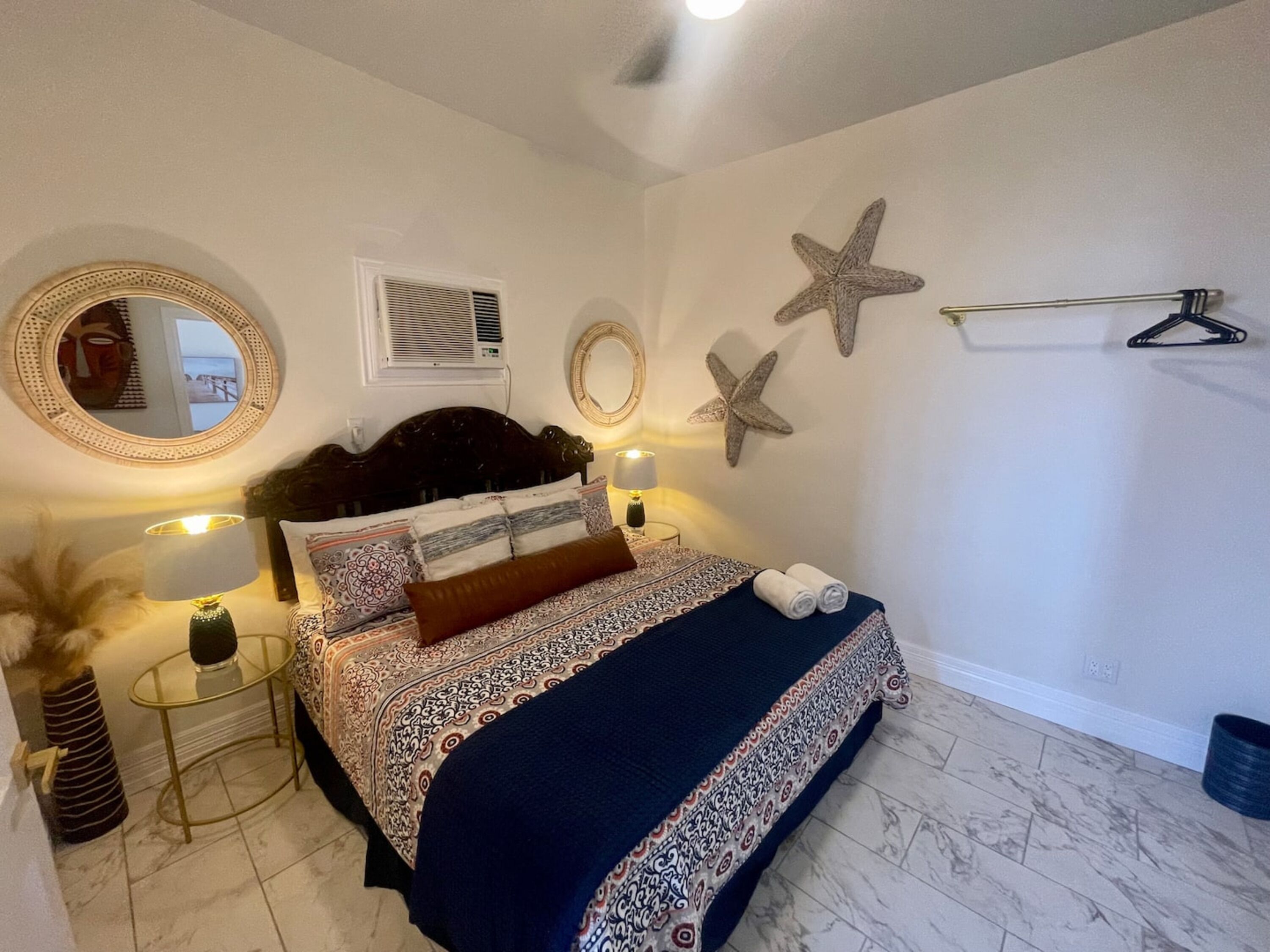 A bedroom with a bed, bedside tables, a mirror, starfish wall decor, and a hanging towel rack.