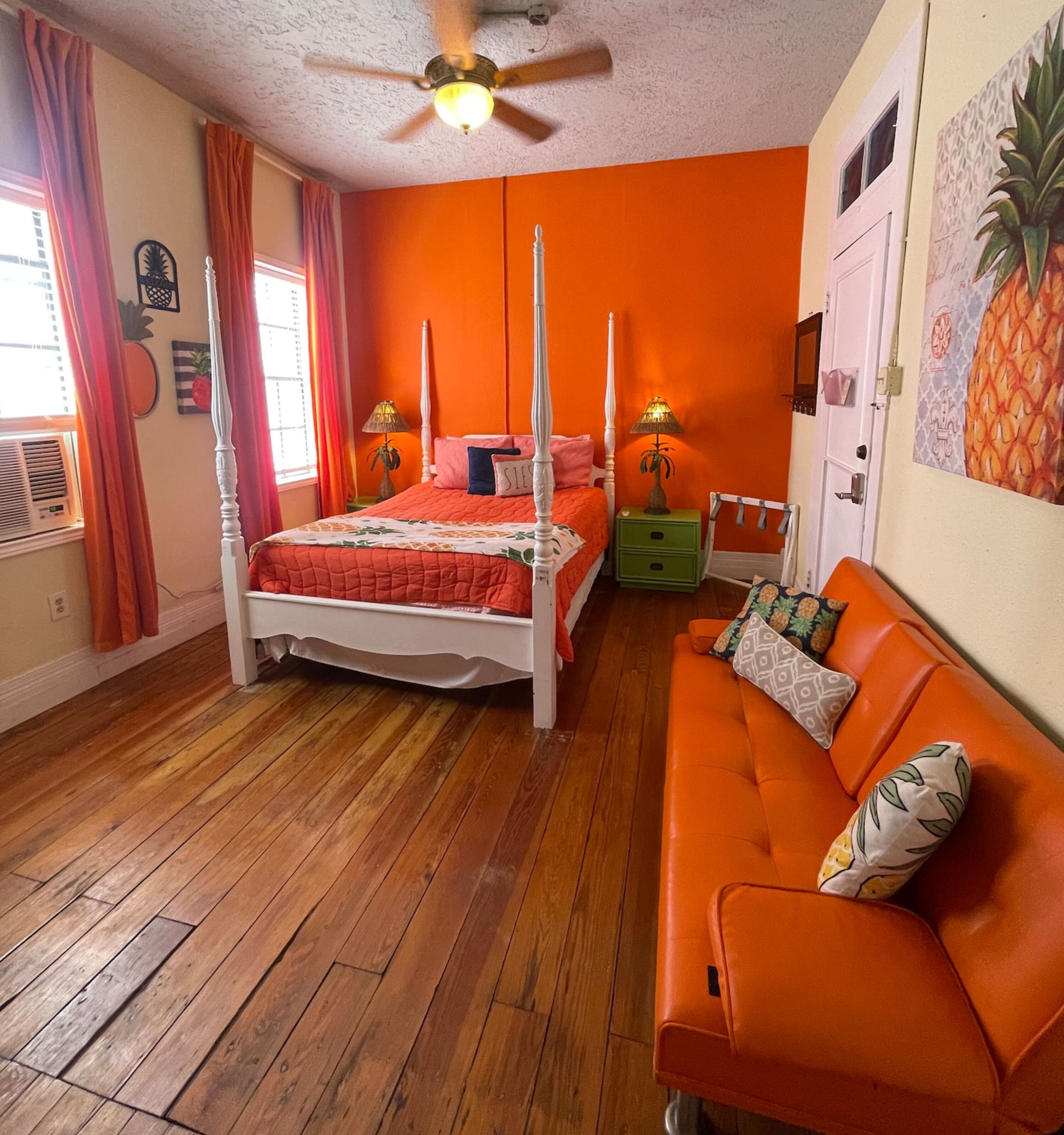A bedroom with a four-poster bed, a wooden floor, an orange sofa, and a ceiling fan.