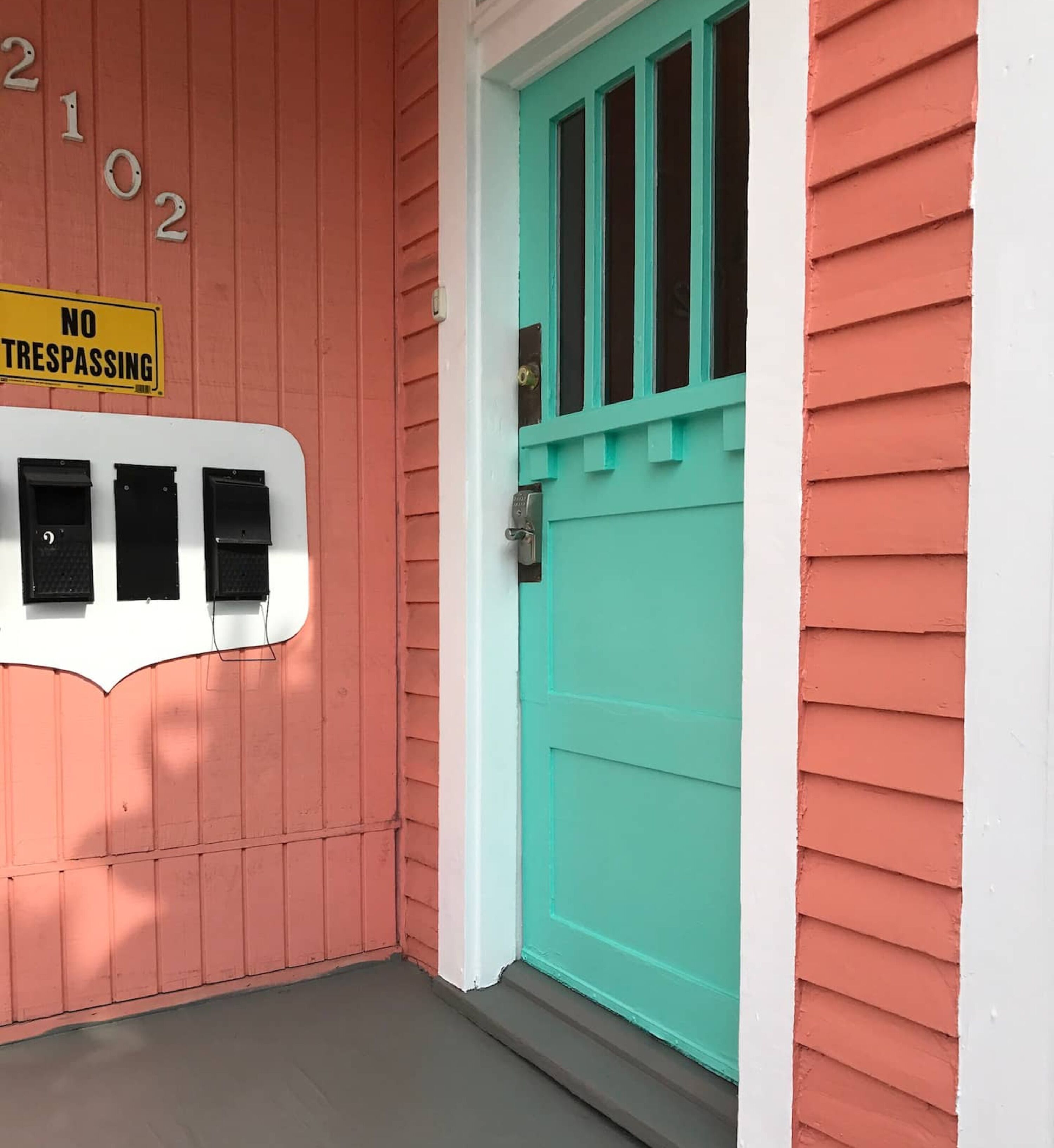 Een huis met een rode gevel, een turquoise deur en een bord met 'NO TRESPASSING'.