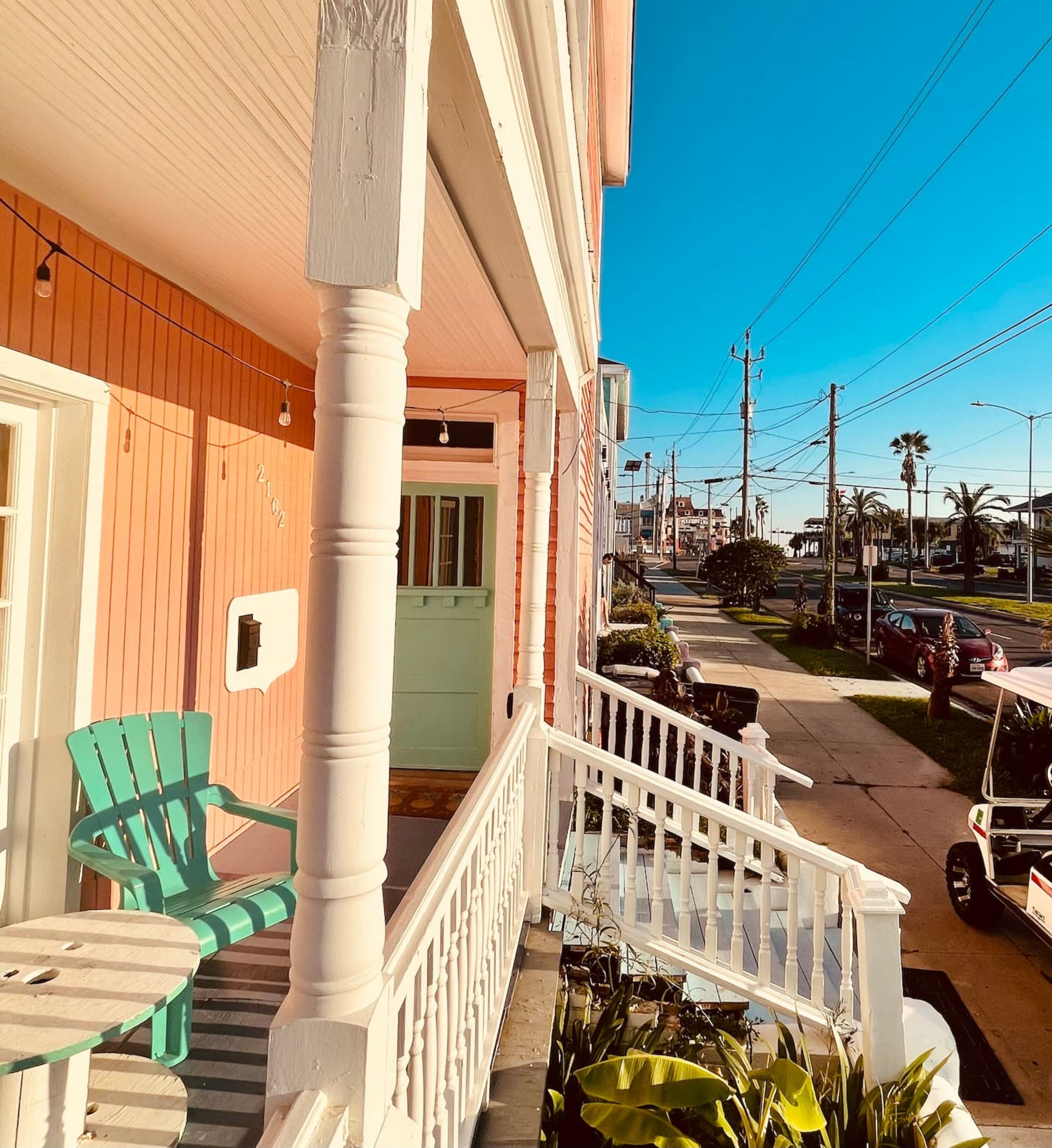 A porch with a green chair, a white railing, and a street view with cars and power lines.