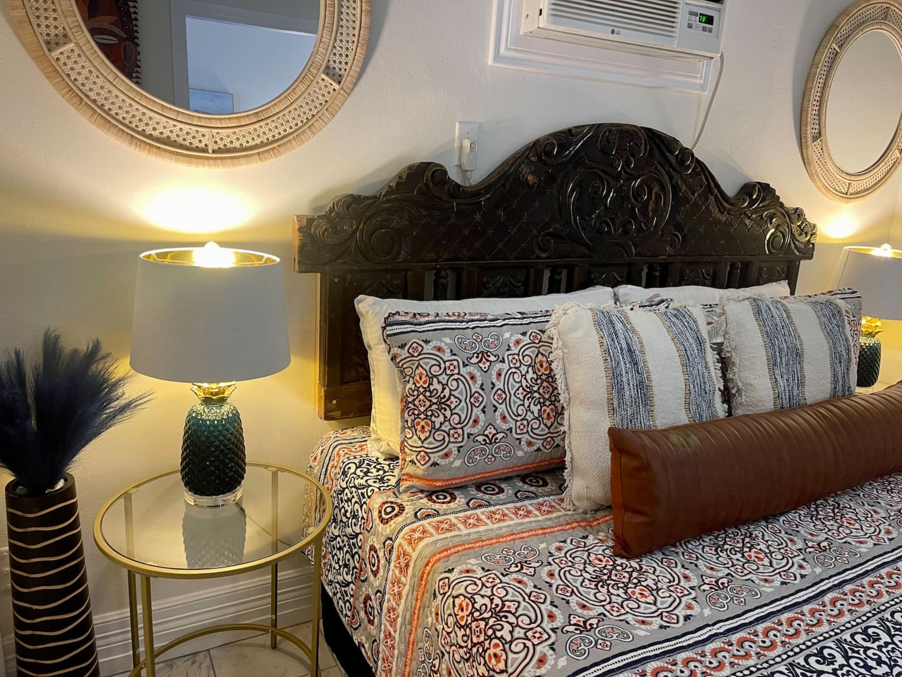 A bedroom with a bed, two bedside tables, a mirror, and a wall-mounted air conditioning unit.