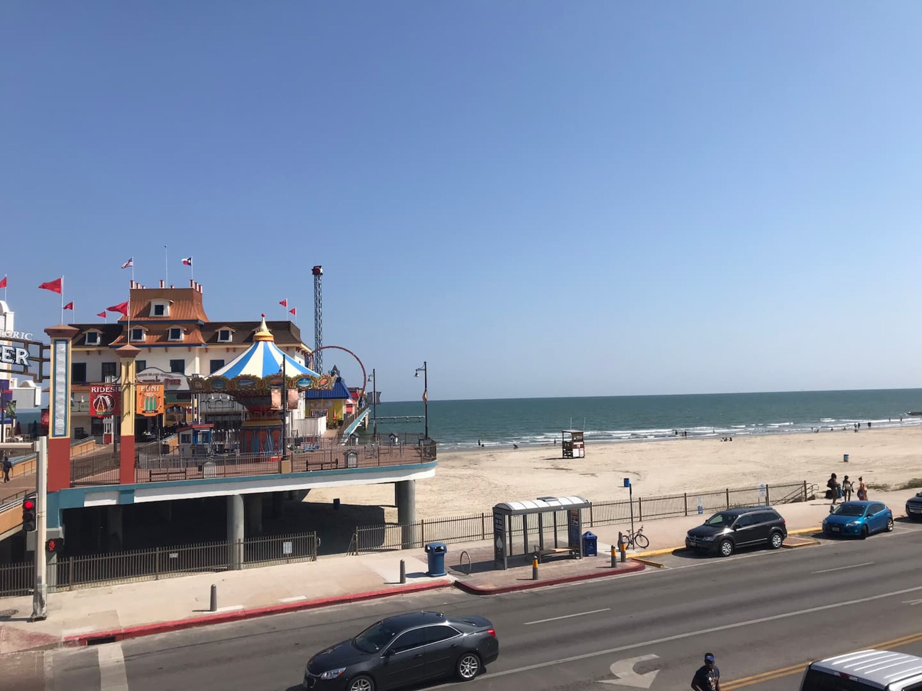 Un edificio frente al mar con un carrusel, una playa al fondo y una carretera con coches.