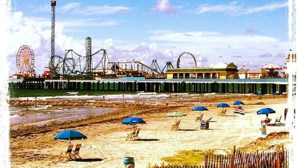 Una playa con sombrillas, un muelle y atracciones de parque de diversiones al fondo.