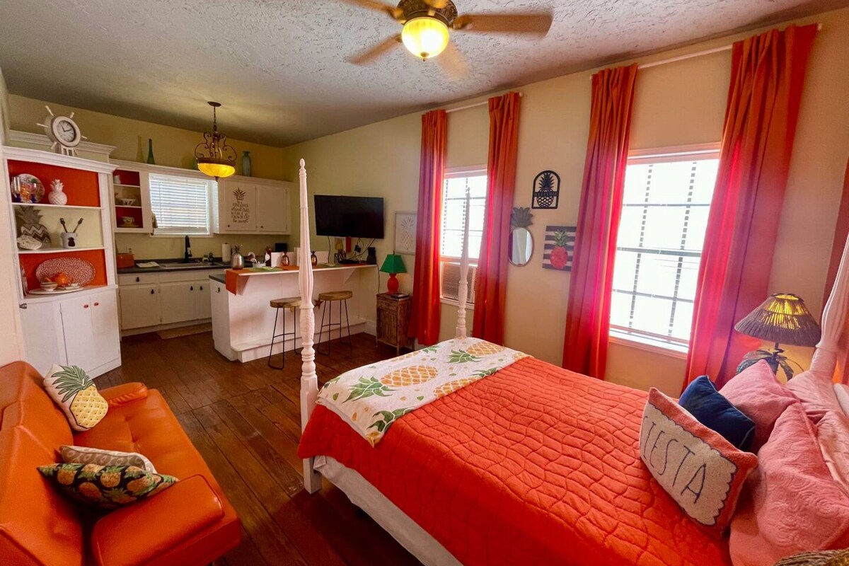 Een slaapkamer met een bed, een bureau, een kitchenette en een badkamer.