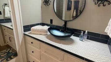 A bathroom with a round mirror, a sink with a blue basin, a towel on the counter, and a decorative octopus rug.