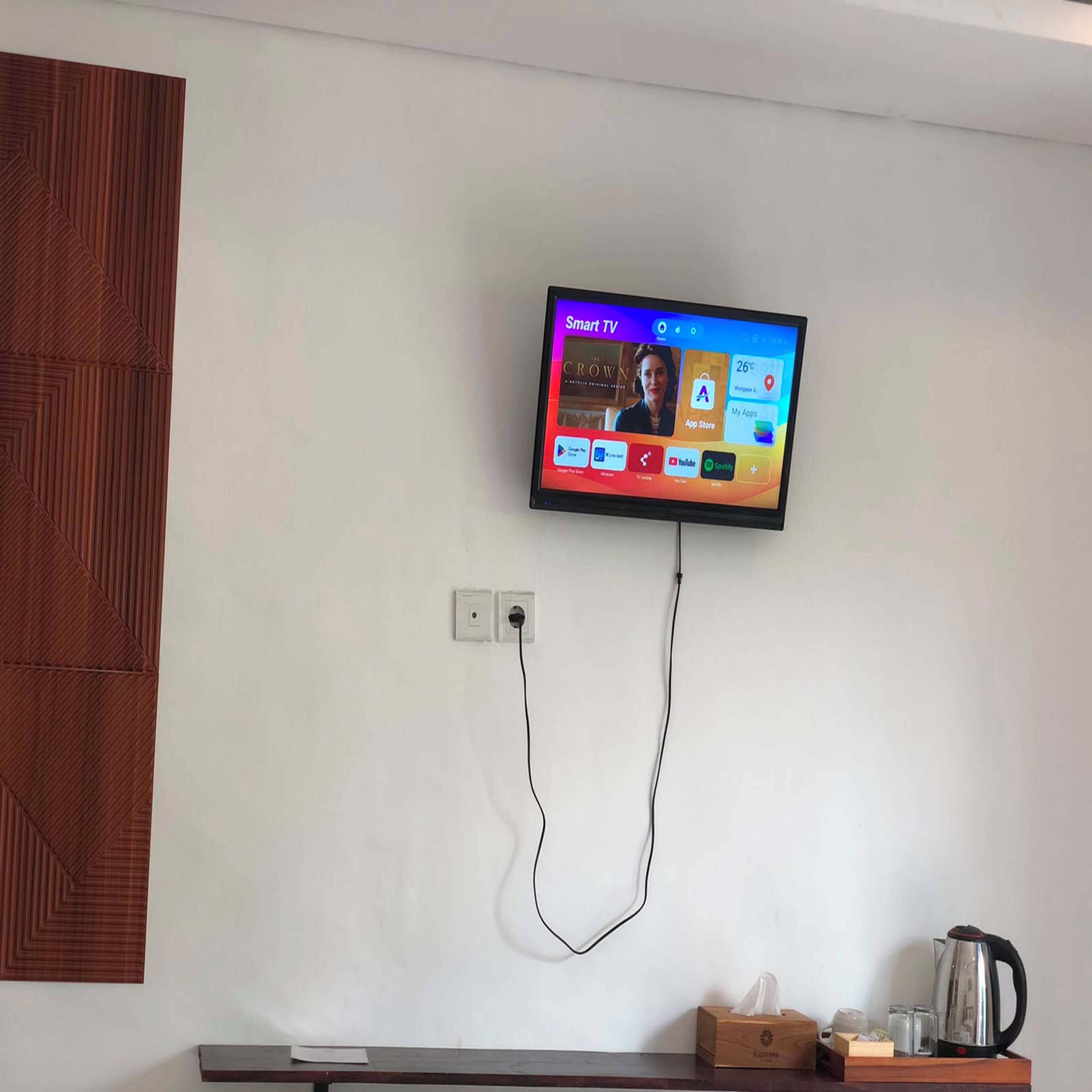 Televisão de tela plana presa a uma parede branca, exibindo interface de Smart TV com diversos aplicativos.