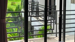A balcony with a metal railing, a staircase, and a view of a green landscape. - Radhana Living (Tampaksiring)