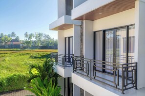 Un bâtiment moderne doté d’un balcon donnant sur un paysage verdoyant et des palmiers.