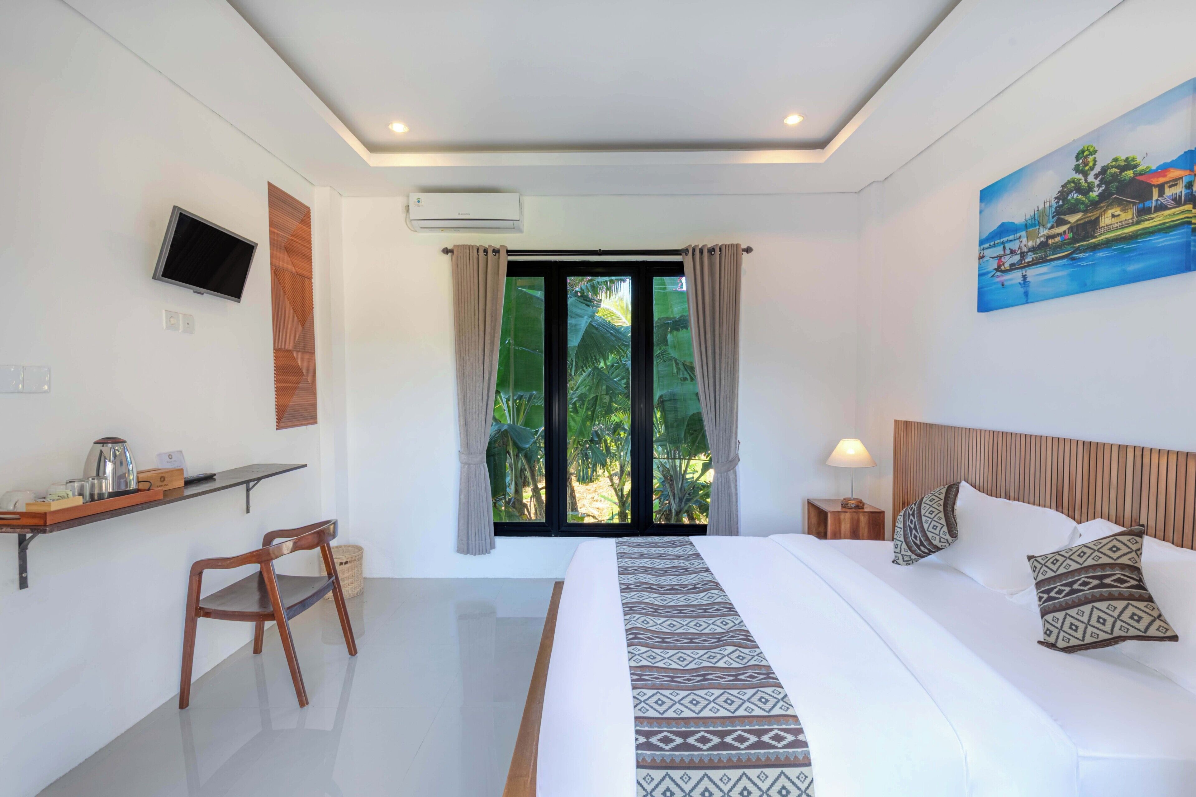 A hotel room with a bed, a desk with a chair, a TV, an air conditioning unit, and a painting on the wall.