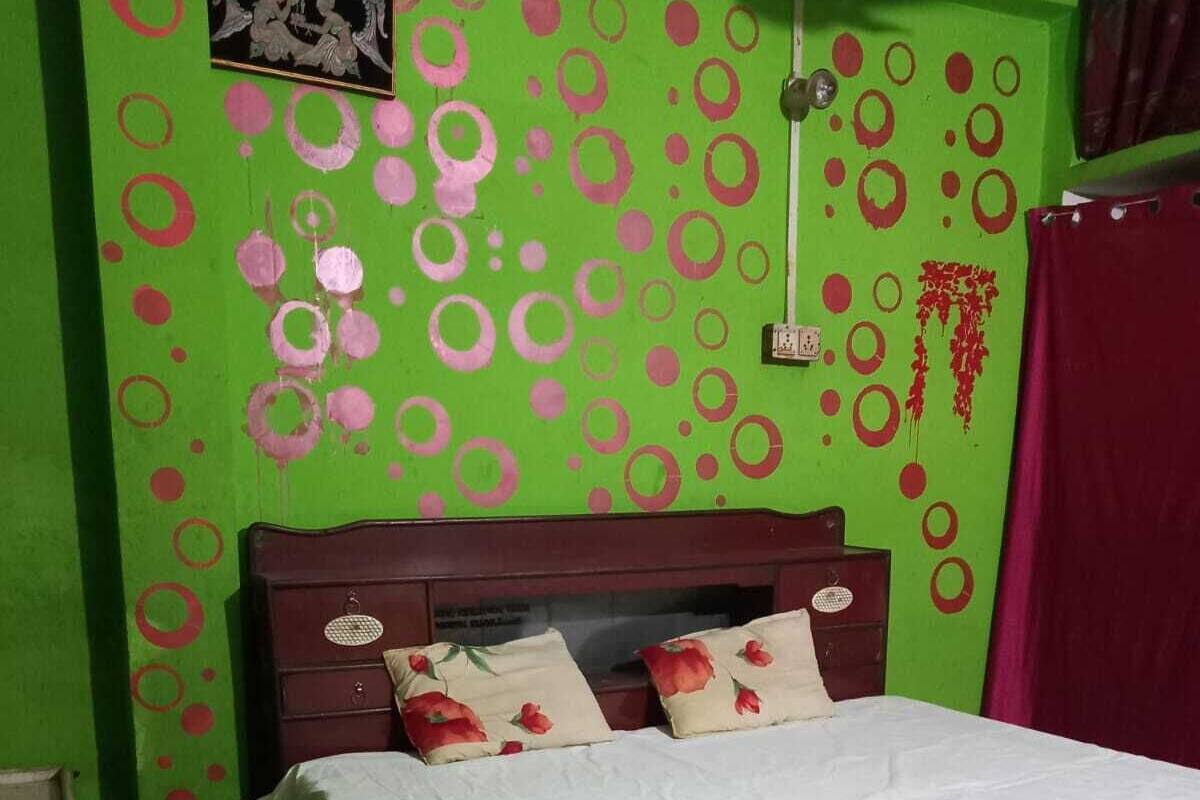Un dormitorio con cama, almohadas, cabecero, pared con diseños circulares y una ventana.