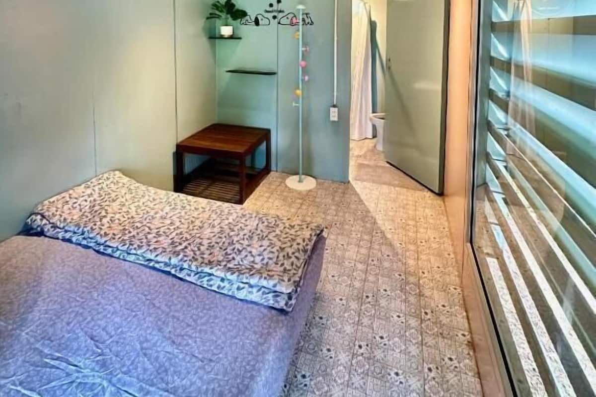 Un dormitorio pequeño con cama, una mesita, una planta en maceta y una puerta corredera que da al baño.
