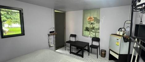 Una habitación con una cama, un escritorio, dos sillas, una mesita, un radiador y una ventana con vistas a zonas verdes.