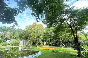 A lush garden with a pond, trees, and a small building.