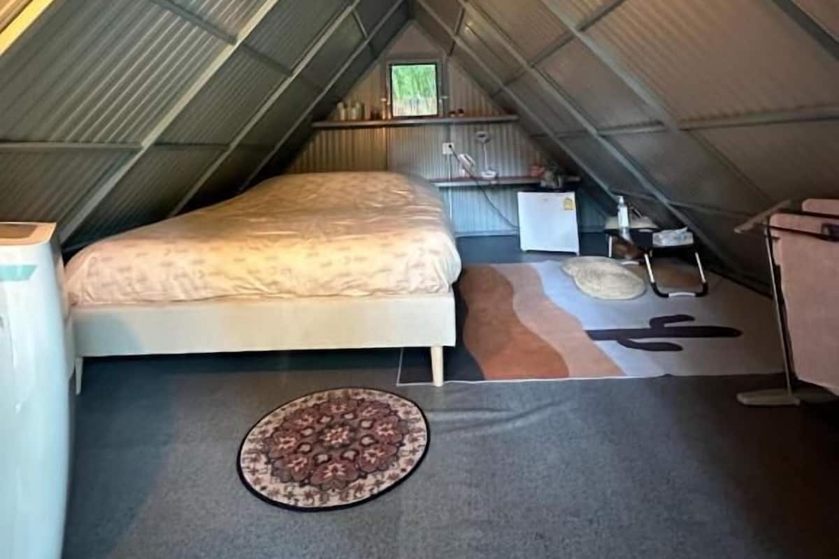 Un dormitorio estilo ático pequeño, con techo inclinado, una cama, una mesita y una silla.