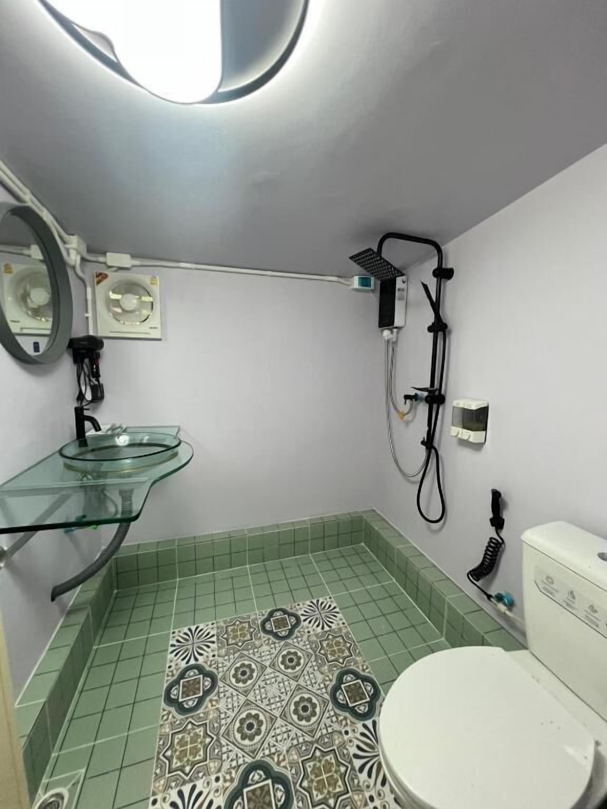 A bathroom with a glass sink, a toilet, a shower, and a ceiling light.
