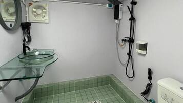 A bathroom with a glass sink, a toilet, a shower, and a ceiling light.