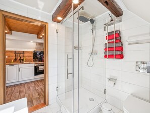 Une salle de bain moderne avec une douche à parois de verre, des carreaux blancs, des toilettes et un porte-serviettes avec des serviettes rouges.