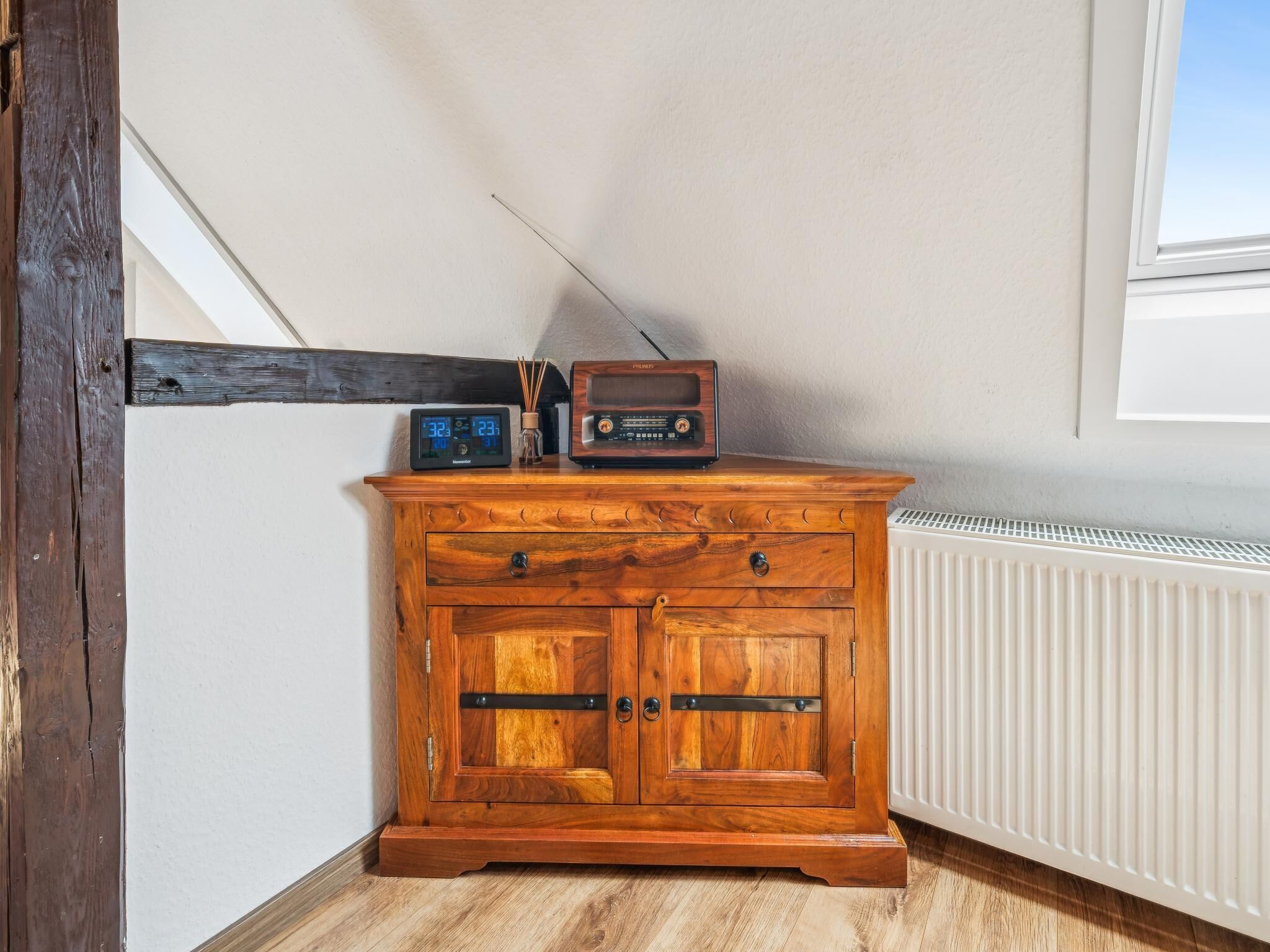 A wooden cabinet with a radio and clock, a radiator, and a window.