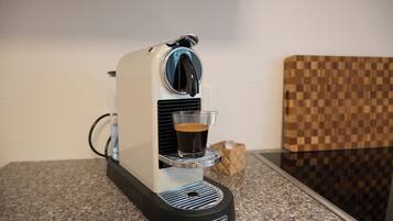 A coffee machine with a glass cup on its drip tray, a power cord, and a checkered wall in the background.