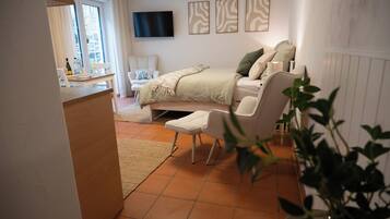 Een slaapkamer met een bed, een stoel, een televisie en een raam.