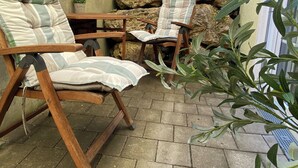 Un patio con dos sillas de madera, una mesa pequeña y un muro de piedra.