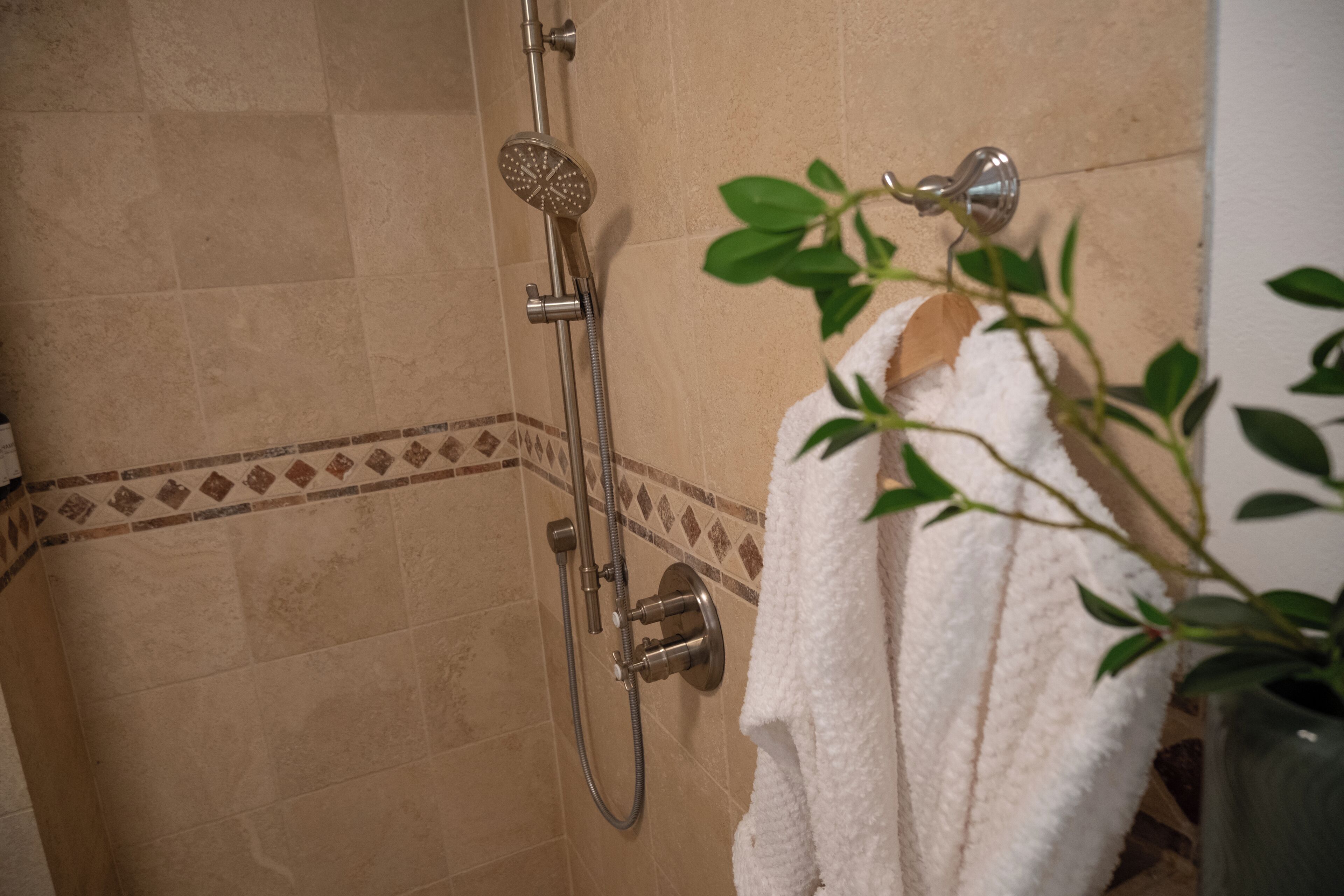 A shower with a handheld showerhead, a wall-mounted control, and a towel hanging on a rack.