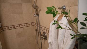 A shower with a handheld showerhead, a wall-mounted control, and a towel hanging on a rack.