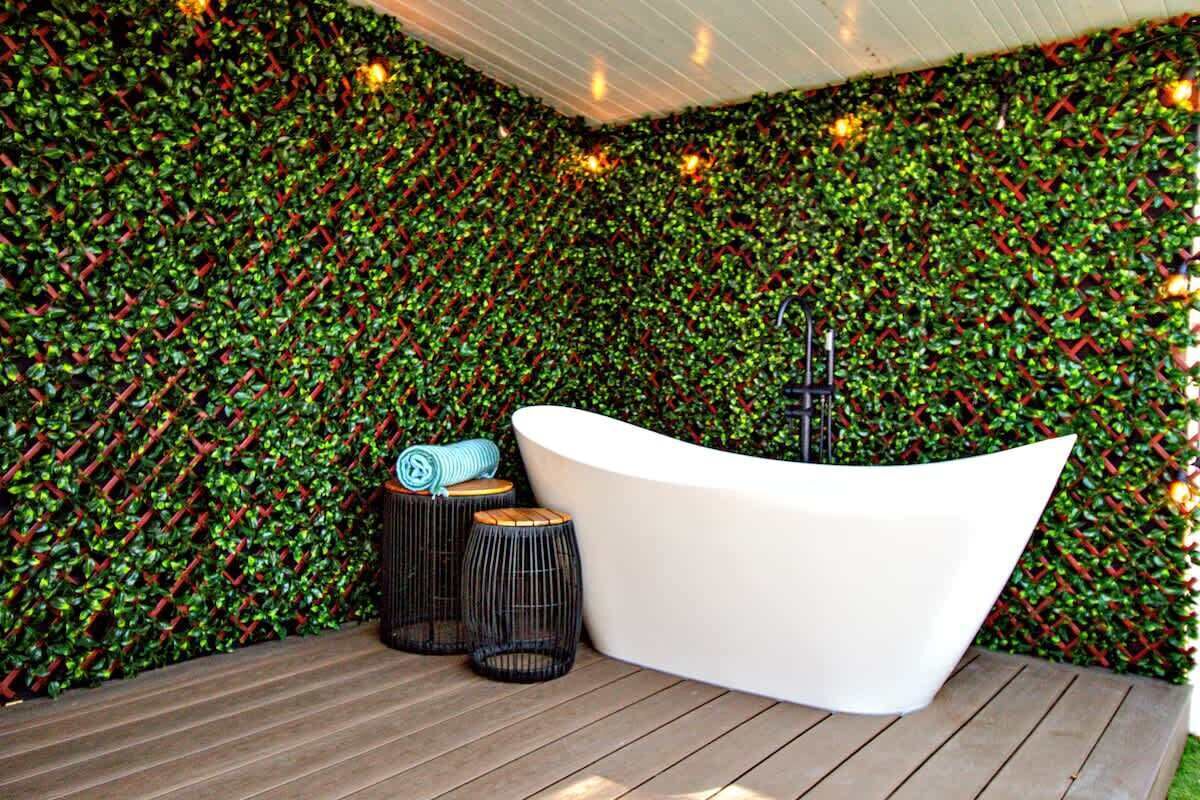 A modern bathroom with a white bathtub, wooden flooring, and a green leafy wall.
