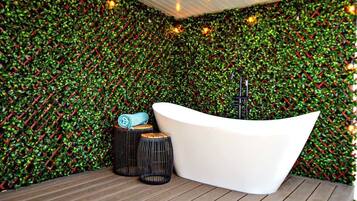 A modern bathroom with a white bathtub, wooden flooring, and a green leafy wall.