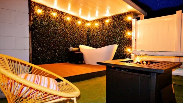 A cozy outdoor seating area with a hammock chair, a white cushioned chair, and a fire pit.