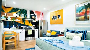 A modern bedroom with a bed, a sofa, a kitchen area, and a dining table.